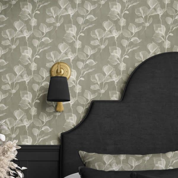 A Gold Wall Sconce With A Black Shade Is Mounted On A Wall With A Light Green Leaf Patterned Wallpaper. A Dark Headboard Is Partially Visible.
