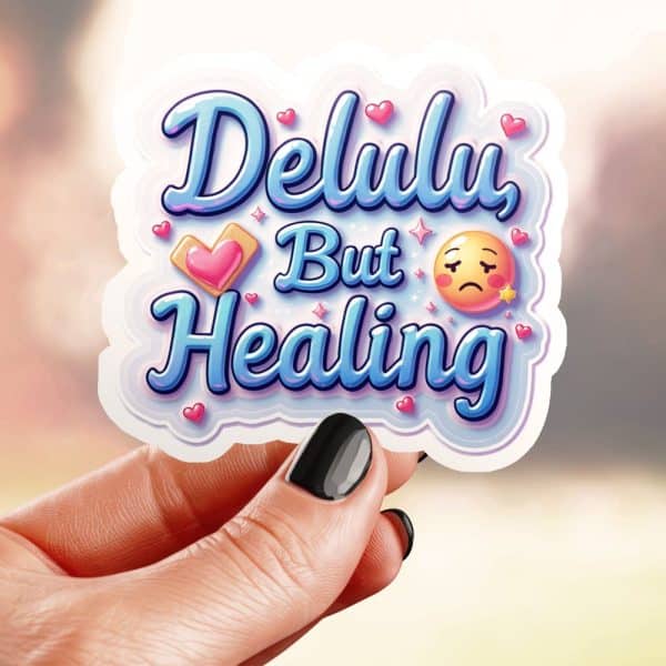 A Hand Holds A Sticker That Says Delulu But Healing In Stylized Blue Lettering, Accompanied By Small Hearts And An Emoticon.