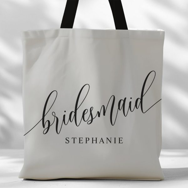 Off-White Tote Bag With Black Handles And The Word Bridesmaid In A Script Font, With The Name Stephanie Underneath.