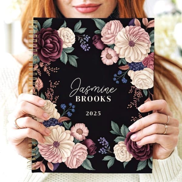 A 2025 Spiral-Bound Planner With A Dark Background And A Floral Design Featuring Burgundy, Blush, And Cream Flowers. The Name Jasmine Brooks Is Printed On The Cover.