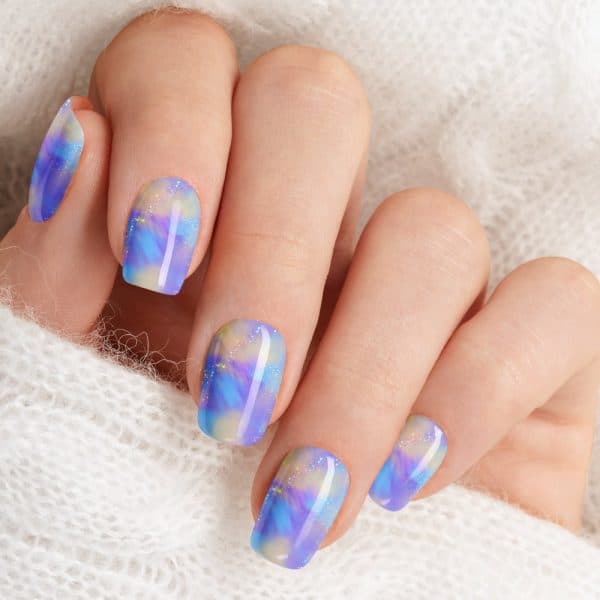 Closeup Of A Hand With Short Nails Featuring A Pastel Purple And Blue Marbled Nail Polish Design.