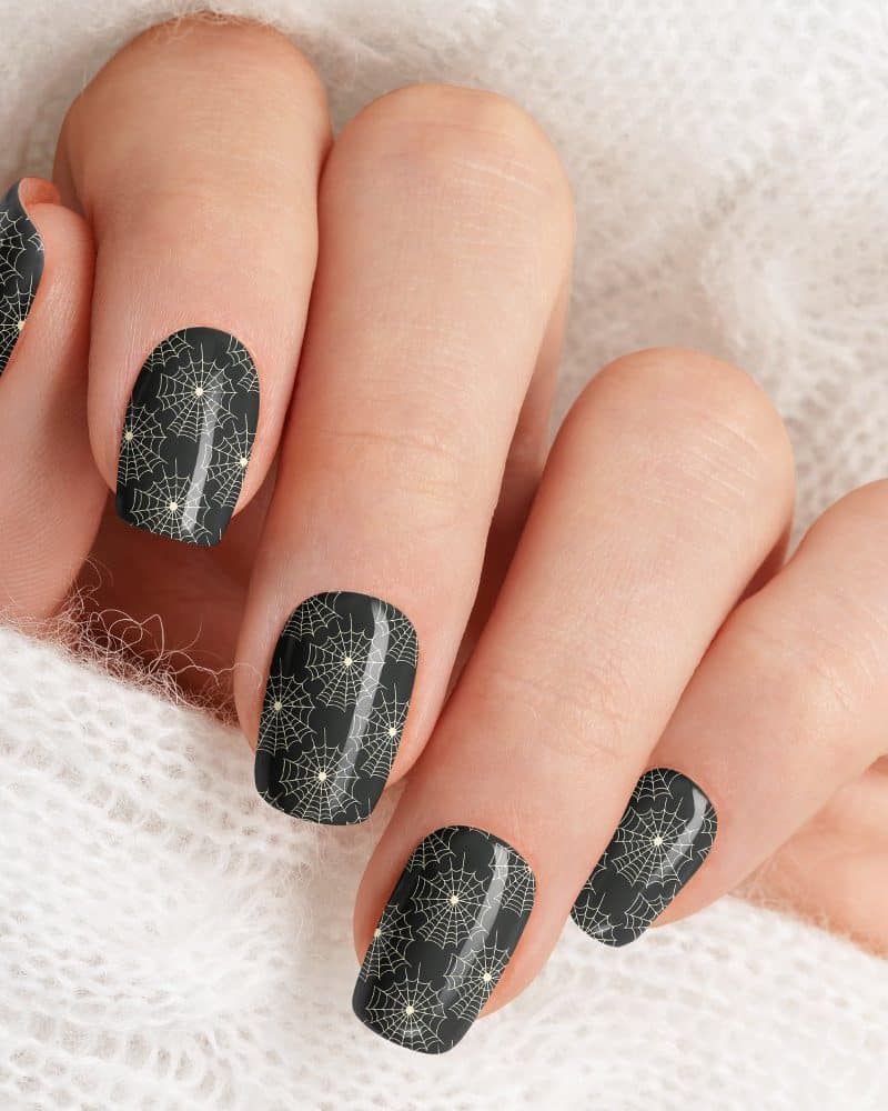 Closeup of a hand with dark nails decorated with a spiderweb pattern.
