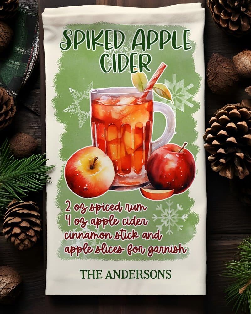 A kitchen towel featuring a watercolor illustration of a mug of spiked apple cider with apples and a recipe.