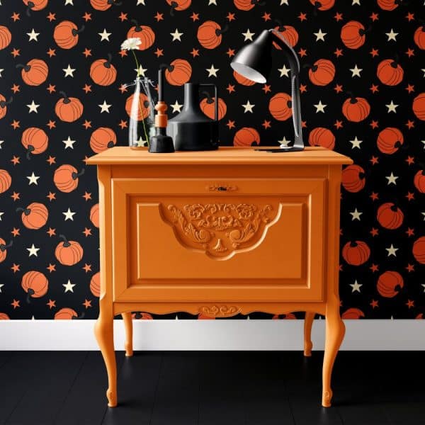 Orange Painted Wooden Cabinet With Ornate Detailing, Against A Black Pumpkin And Star Patterned Wall.