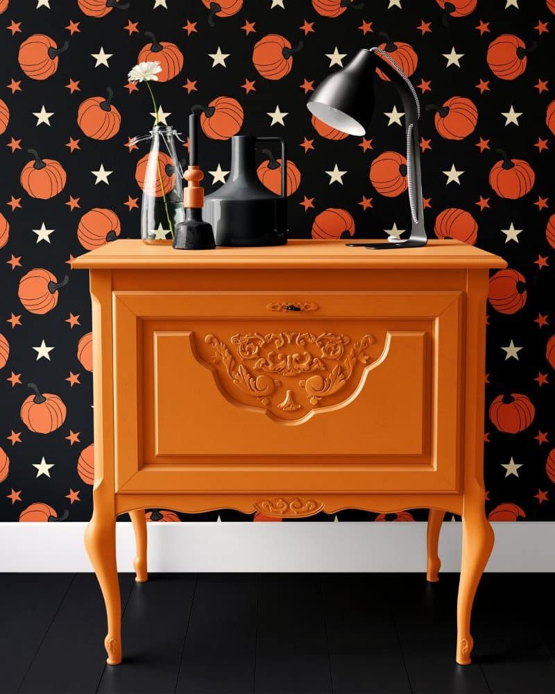 Orange painted wooden cabinet with ornate detailing, against a black pumpkin and star patterned wall.