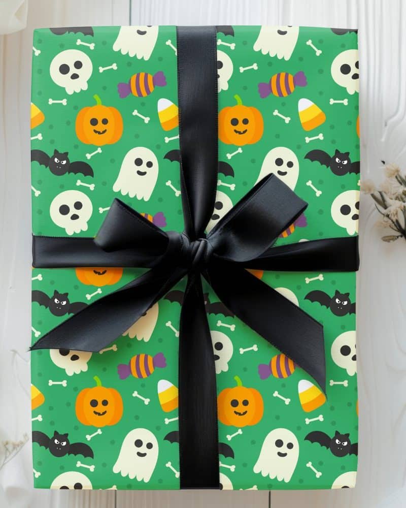 Halloween gift wrapped in green paper with a black ribbon. The wrapping paper features ghosts, pumpkins, candy corn, and skulls.