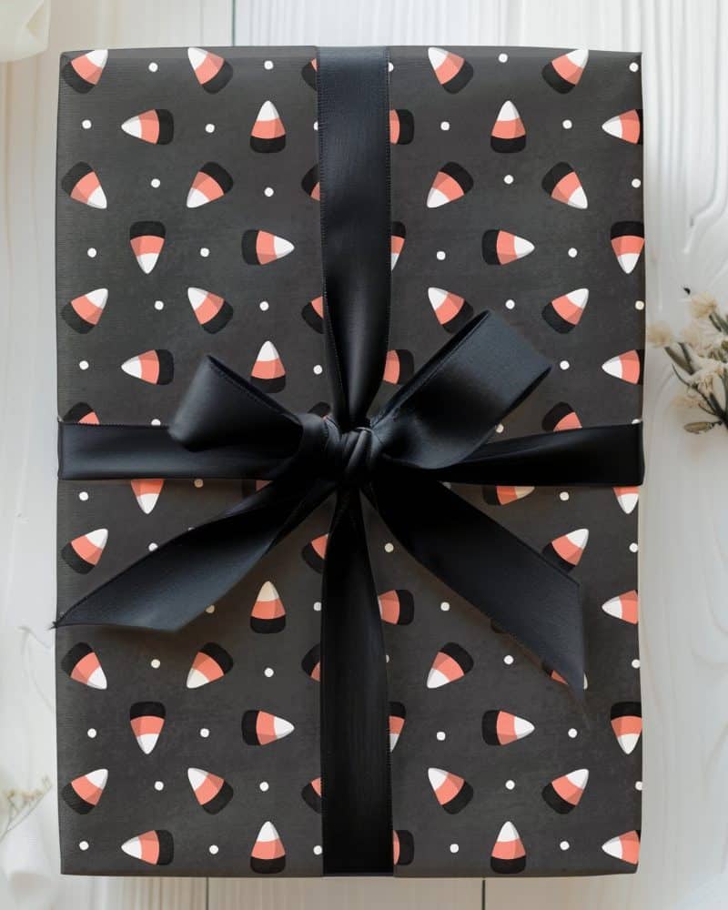 A gift wrapped in dark gray paper with a candy corn pattern and tied with a black ribbon.