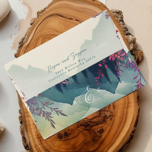 Wedding Invitation With Watercolor Mountain Landscape And Floral Details. The Names Regan And Zayyan Are Displayed.