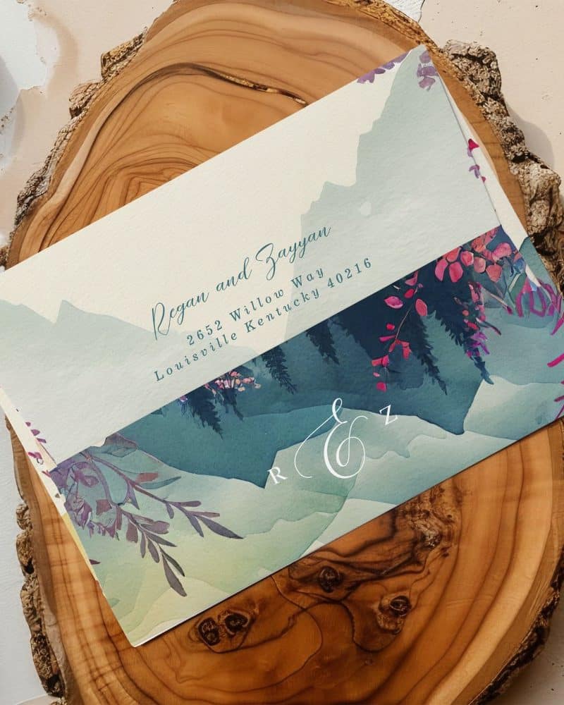 Wedding invitation with watercolor mountain landscape and floral details. The names Regan and Zayyan are displayed.