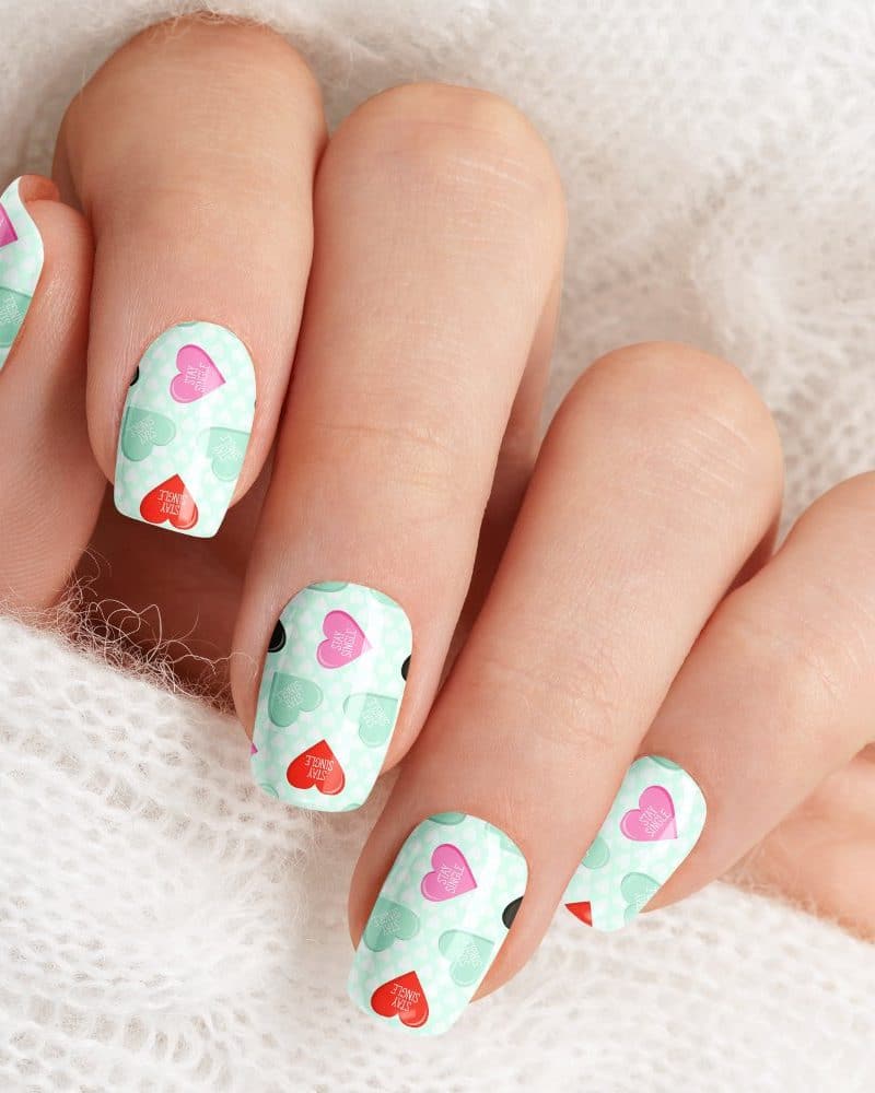 Close-up of a hand with fingernails decorated with a pattern of mint green and pink hearts that say Stay Single.