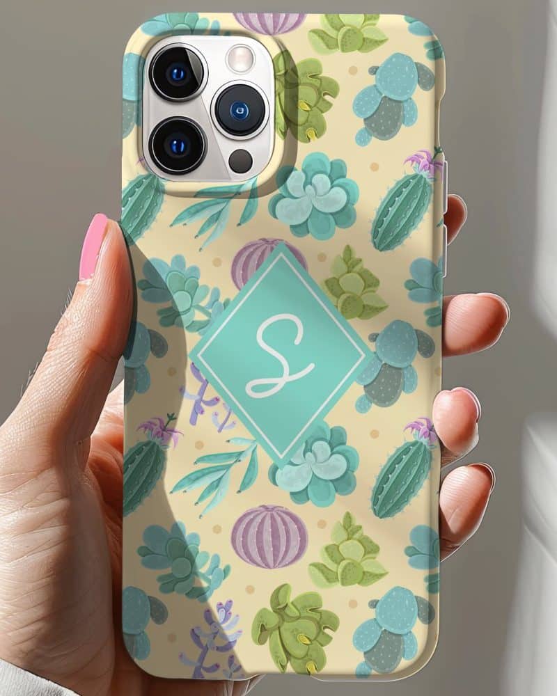 Hand holding a pale yellow iPhone case featuring a pattern of cacti and succulents, and a teal monogram.