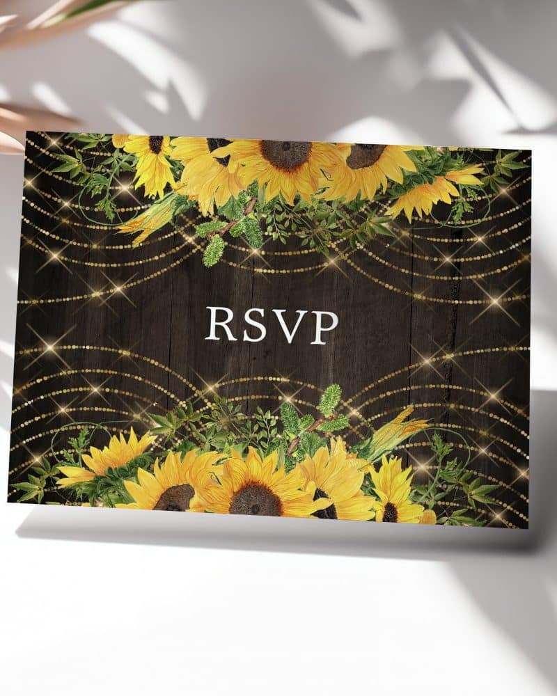 RSVP card with sunflowers and gold string lights on a dark wood background.