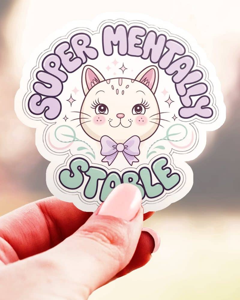 A hand holds a sticker featuring a cute cartoon cat wearing a bow, surrounded by text that says Super Mentally Stable.