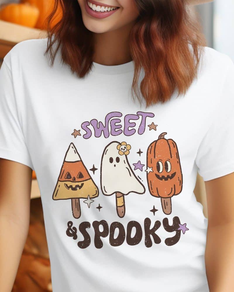 Woman wearing a white t-shirt featuring a Halloween design of candy corn, ghost, and pumpkin pops.