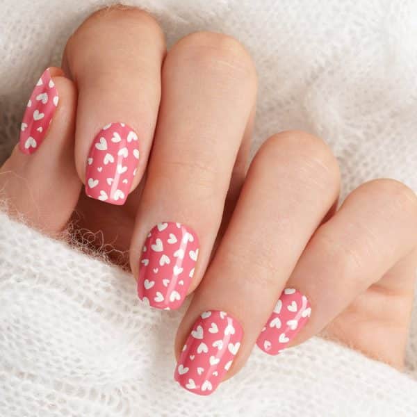 Close-Up Of A Hand With Pink Nails Decorated With Small White Hearts.