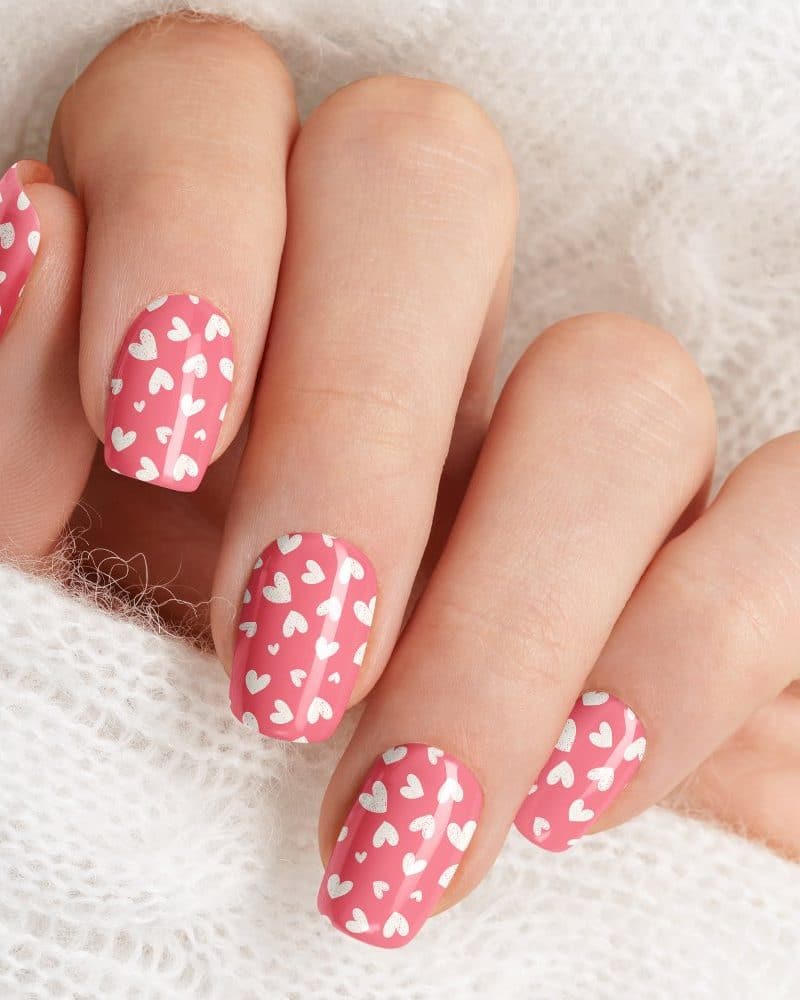 Close-up of a hand with pink nails decorated with small white hearts.