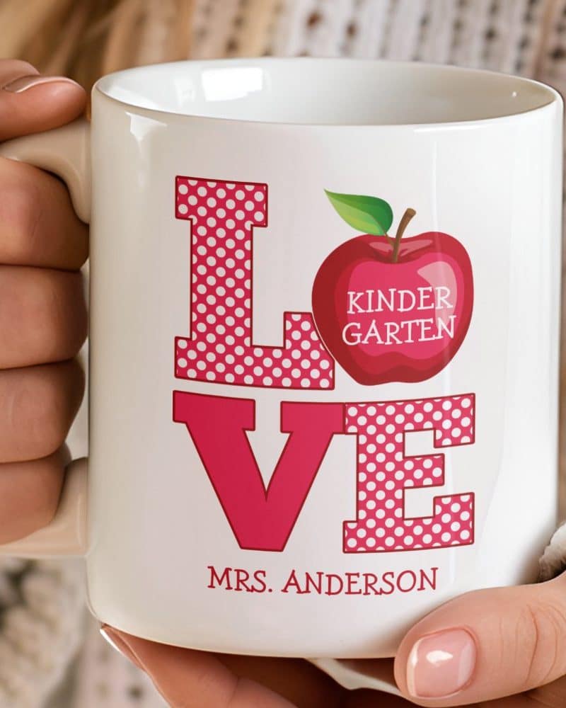 White coffee mug with pink polka dot LOVE graphic, a red apple with Kindergarten text, and Mrs. Anderson's name.