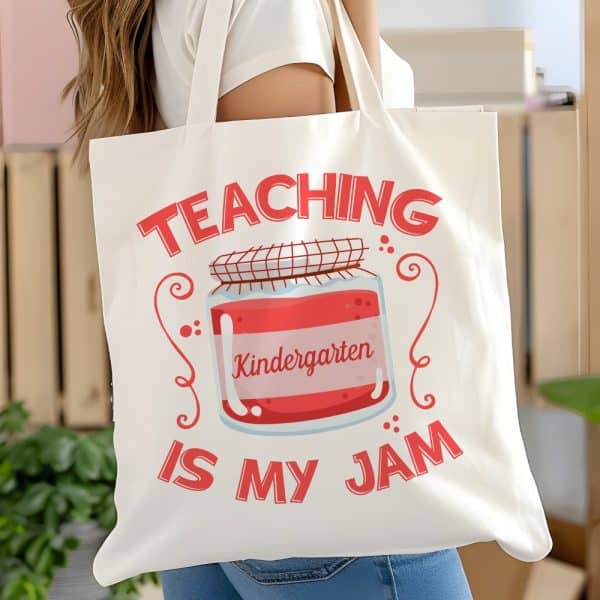 White Tote Bag With Red Text And Illustration Of A Jar Of Jam Labeled Kindergarten. The Text Reads Teaching Kindergarten Is My Jam.