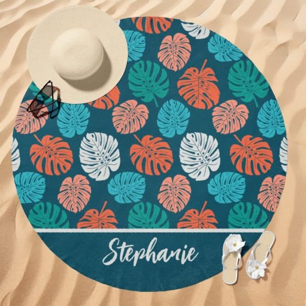 Round Beach Towel With A Teal Background And A Repeating Pattern Of Colorful Monstera Leaves. The Name Stephanie Is Printed At The Bottom.