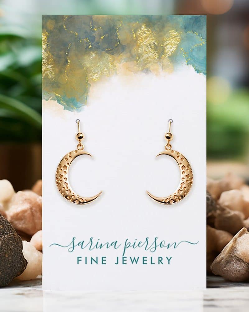 Gold crescent moon earrings displayed on a jewelry card.