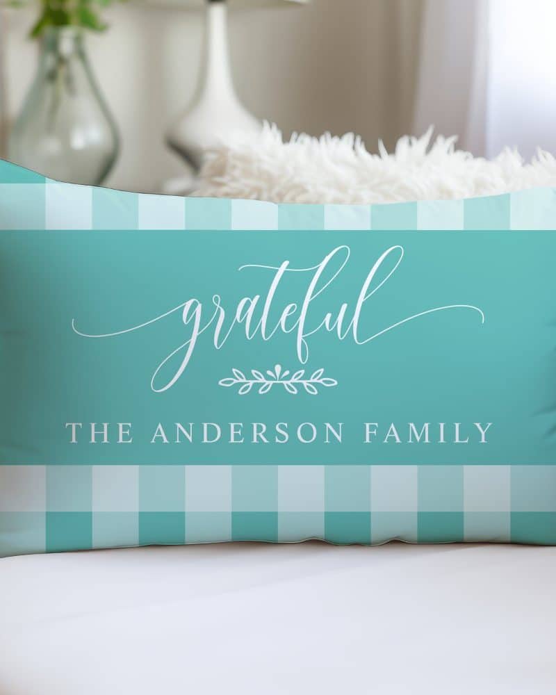 Teal rectangular pillow with a white gingham border and the word grateful in a script font, along with the text The Anderson Family.