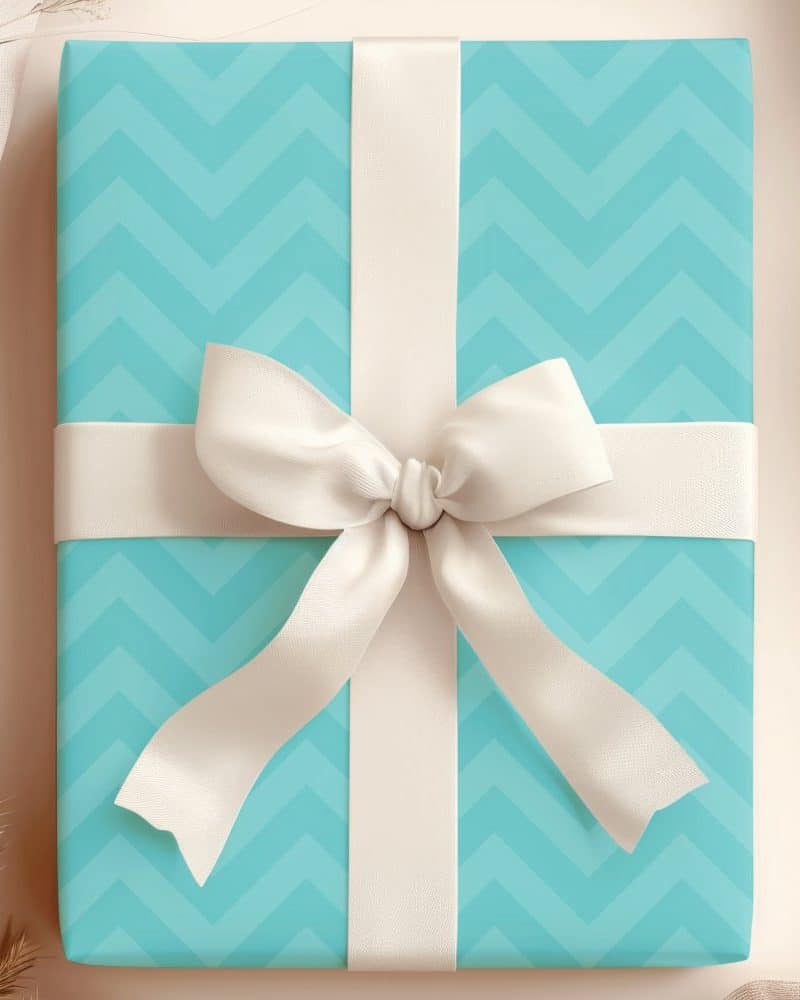 A light teal gift box with a chevron pattern, topped with a large off-white bow.