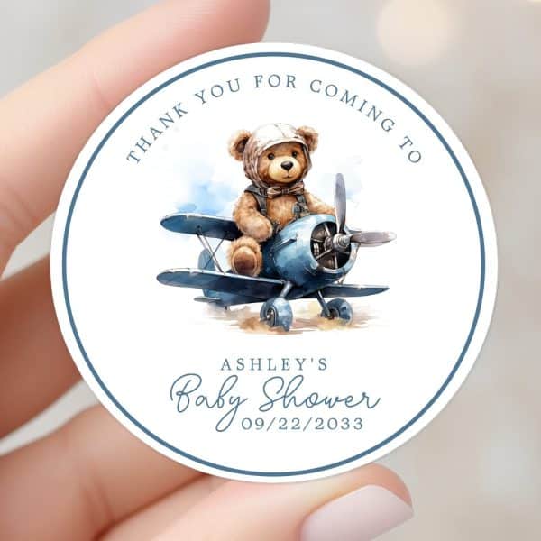 Round Baby Shower Thank You Sticker Featuring A Teddy Bear In A Pilot'S Hat Flying A Blue Airplane.