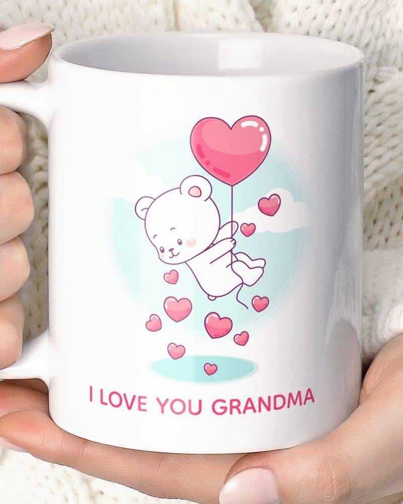 White coffee mug featuring a cartoon white bear holding a heart-shaped balloon, surrounded by smaller hearts. Text at the bottom reads I LOVE YOU GRANDMA.