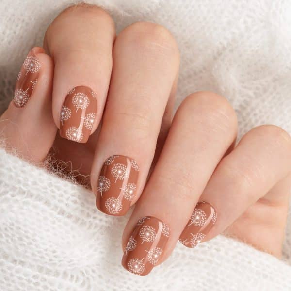 Closeup Of A Hand With Light Brown Nails Decorated With A White Dandelion Pattern.