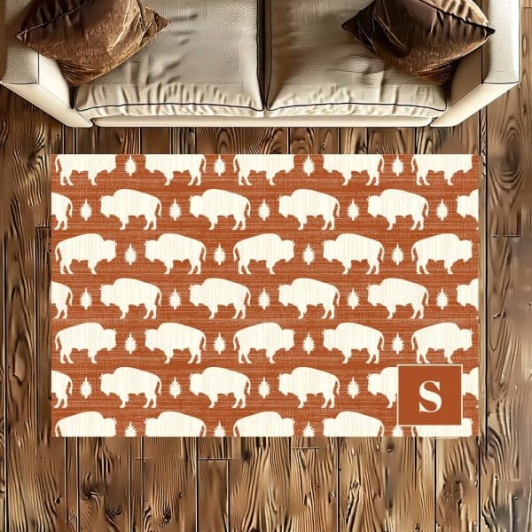 Area Rug With A Repeating Pattern Of White Buffalo Silhouettes On A Rust-Colored Background. A Monogrammed &Quot;S&Quot; Is In The Lower Right Corner.