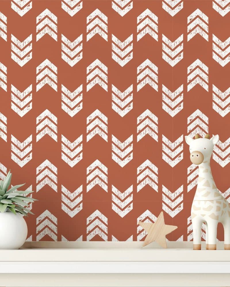 A terracotta-colored wall with a repeating pattern of white distressed chevron arrows, featuring a small giraffe toy and a succulent plant on a shelf in front.