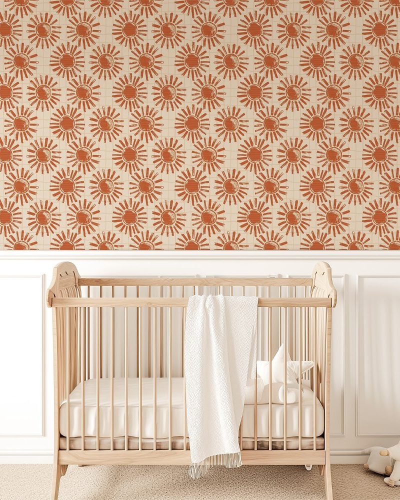 Light wood crib in front of a wall covered in a repeating terracotta sun pattern wallpaper.