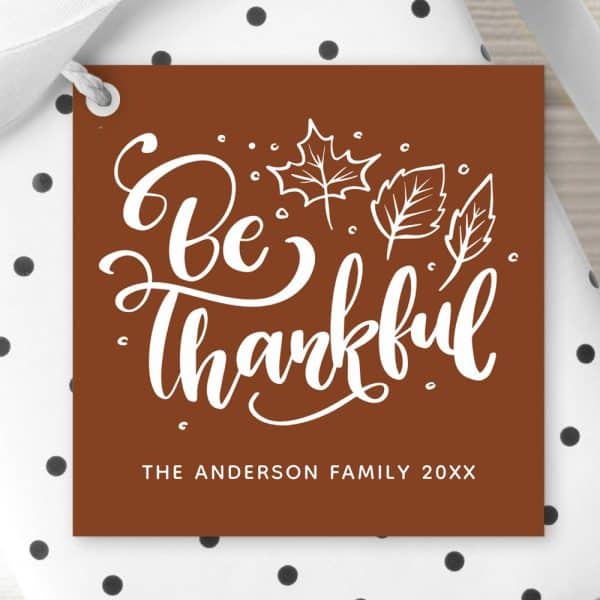 Brown Gift Tag With White Cursive Text That Says Be Thankful, Surrounded By Simple Leaf Drawings. The Anderson Family 20Xx Is Printed At The Bottom.