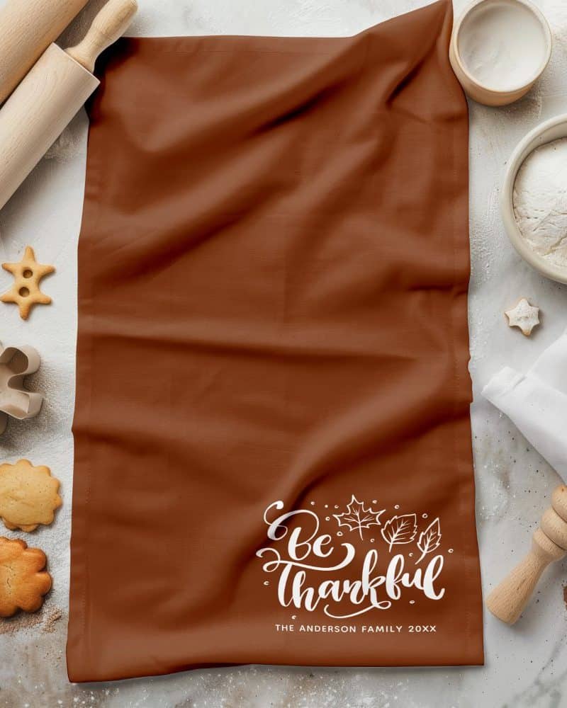 Brown kitchen towel with the text Be Thankful and autumn leaves, personalized with a family name and year.