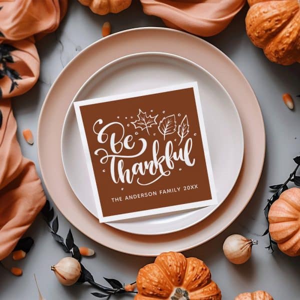 Brown Place Card On A Dinner Plate That Says Be Thankful With The Anderson Family Name And Year.