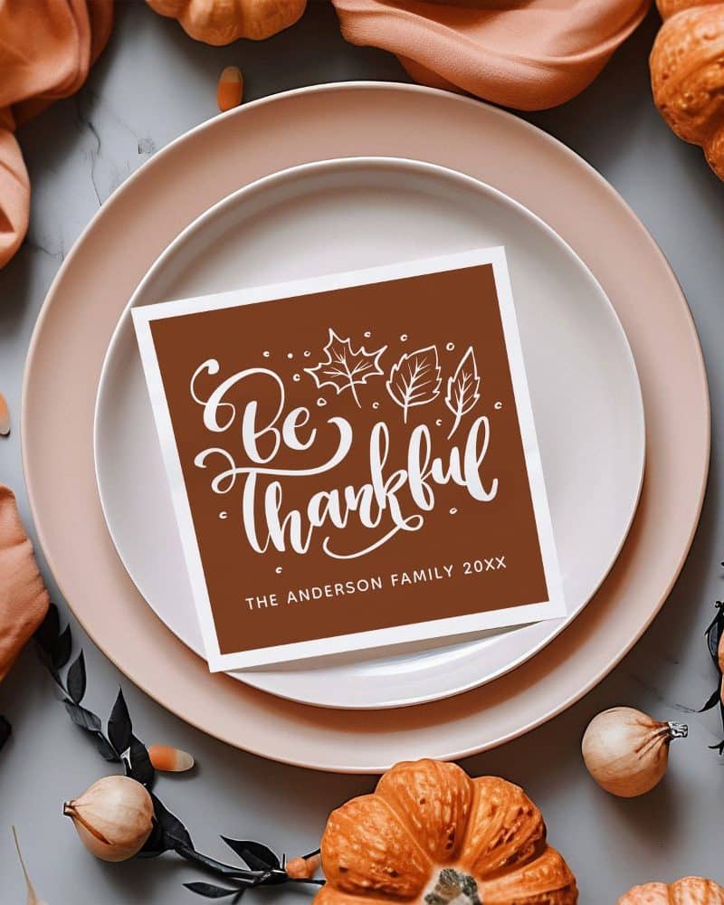 Brown place card on a dinner plate that says Be Thankful with the Anderson family name and year.