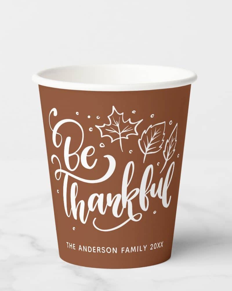 Brown paper cup with white lettering that says Be Thankful and autumn leaves. The Anderson family name and year are at the bottom.