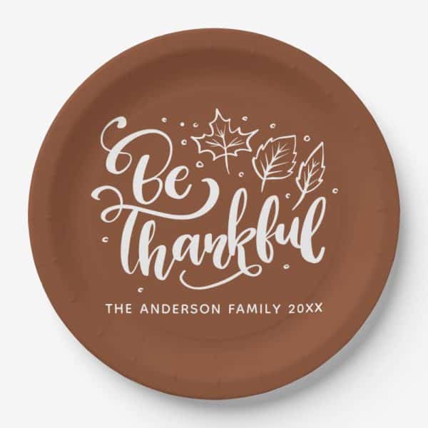 Brown Paper Plate With White Cursive Lettering That Says Be Thankful, And Simple Leaf Illustrations.