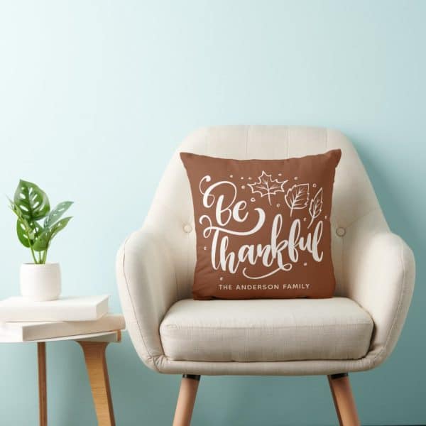 Brown Throw Pillow With White Lettering That Says Be Thankful And The Anderson Family. Autumn Leaves Are Also On The Pillow.
