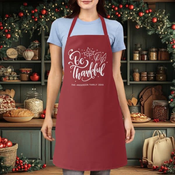 A Maroon Apron With The Text Be Thankful And A Family Name.