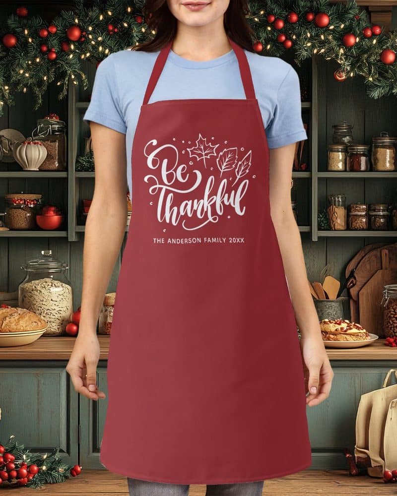 A maroon apron with the text Be Thankful and a family name.