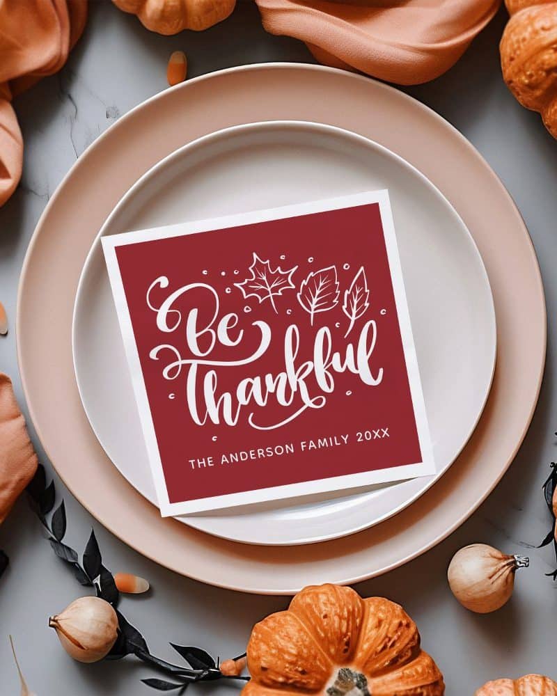 A maroon place card with white lettering reading Be Thankful and the Anderson Family.