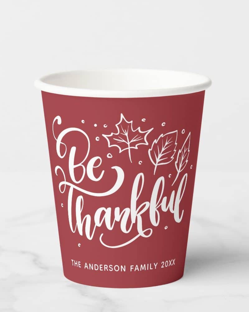 Red paper cup with white lettering that says Be Thankful and has a leaf design. The Anderson family is printed at the bottom.