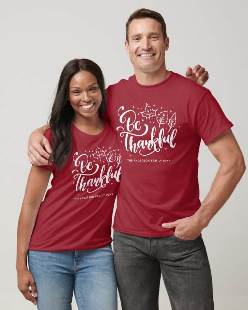 Couple wearing matching red t-shirts with a white "Be Thankful" design and family name.