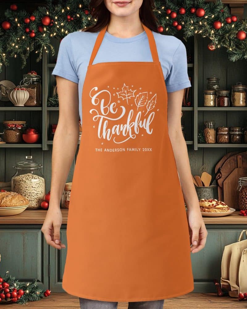 Orange apron with white lettering that says Be Thankful and a family name.