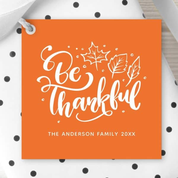 Orange Thanksgiving Gift Tag With White Script That Says Be Thankful And Simple Leaf Illustrations. The Anderson Family Name And Year Are Also Included.