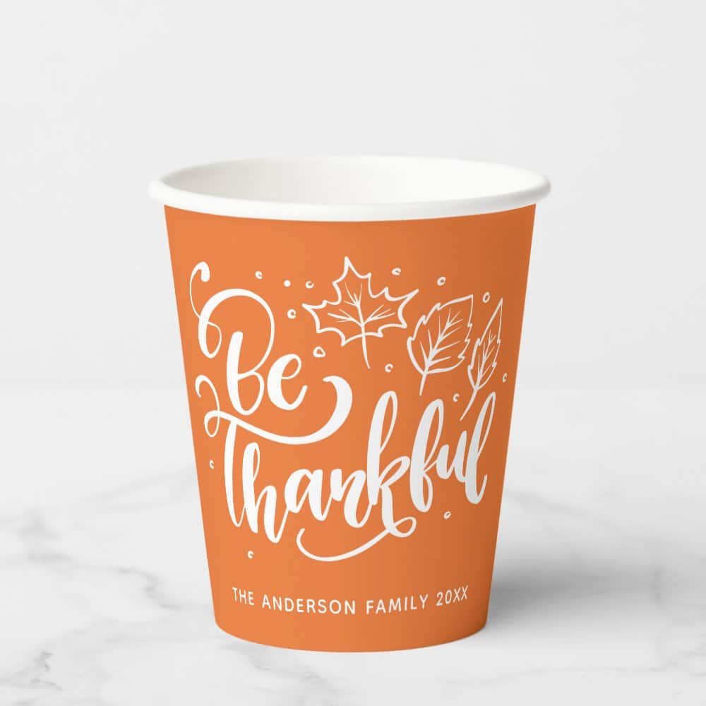 Orange Paper Cup With White Lettering That Says Be Thankful And Includes A Simple Leaf Design.
