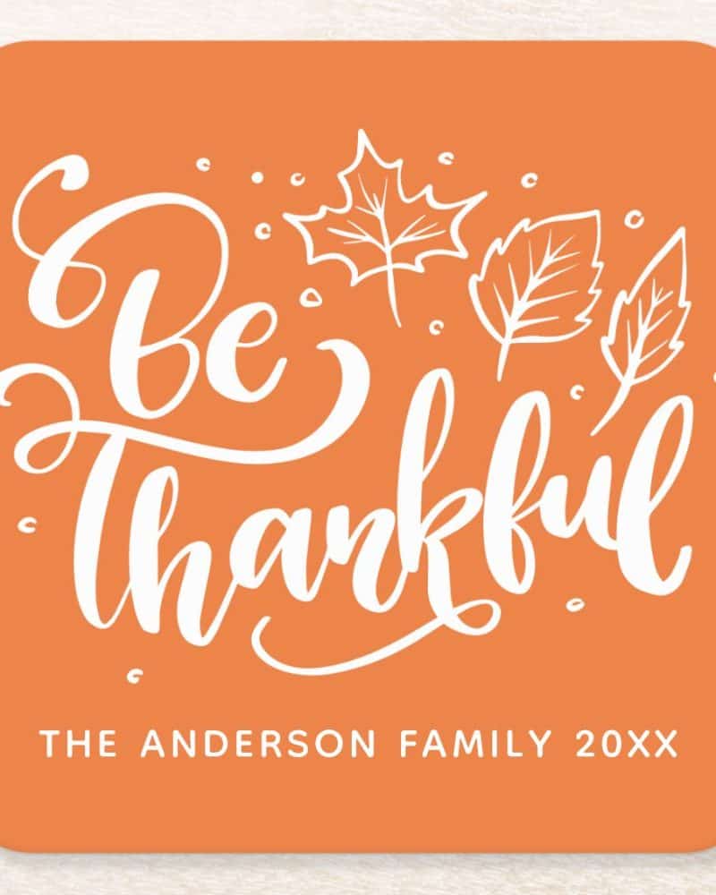 Orange square with white cursive text saying Be Thankful and simple white leaf drawings.