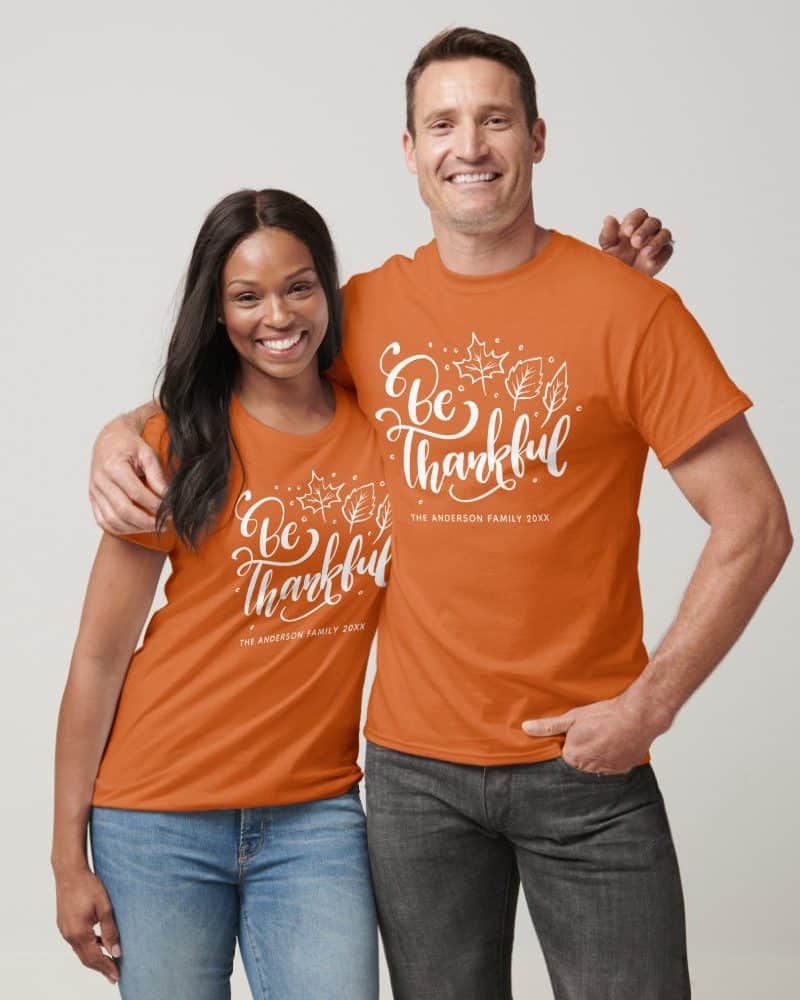 Couple in matching burnt orange t-shirts with a white "Be Thankful" design and family name.