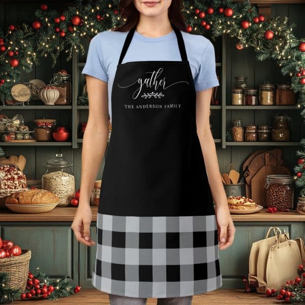 A Person Wearing A Black Apron With A Gray And Black Buffalo Plaid Bottom. The Apron Says Gather, The Anderson Family.